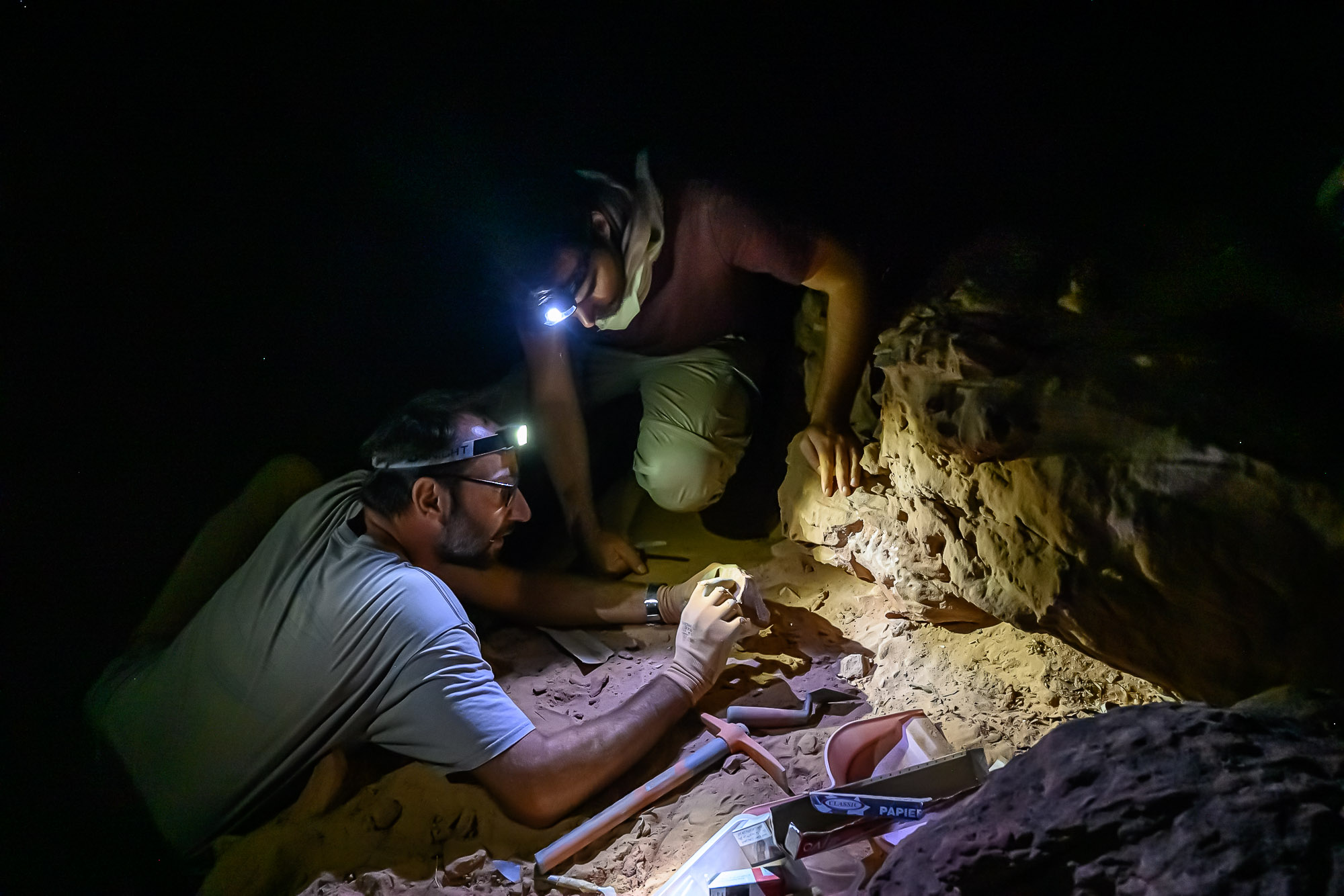 Arabie Saoudite, Al Jawf, Sakaka, Camel Site. Prélévement d'échantillon sur   un rocher provenant d'un des massifs  sculptés afin d'en daté la chute par la technique dite OSL (luminescence stimulée optiquement) . Ce procédé qui consiste à prélever une partie de la roche non exposée à la lumière du jour permet de recueillir et de mesurer en laboratoire la lumière fossile datant d'avant l'évènement, quand le bloc rocheux était encore en place sur le massif. Ce prélèvement doit se faire dans l'obscurité. Sur cette photographie les scientifiques peuvent utiliser une lampe à lumière blanche car ils prélèvent un échantillon témoin exposé à la lumière du jour contemporaine afin de comparer sa photoluminescence à l'échantillon à dater.

Saudi Arabia, Al Jawf, Sakaka, The Camel Site. The prehistorian Remy Crassard and the archeologist Guillaume Charloux are taking samples from a rock from one of the sculpted massifs in order to date the fall by the so-called OSL technique (optically stimulated luminescence). This process, which consists of taking a part of the rock not exposed to daylight, enable to collect and measure, in the laboratory, the fossil light that it stored before its fall. This sample must be taken in the dark. In this photograph, scientists can use a white light lamp as they take a control sample exposed to contemporary daylight in order to compare its photoluminescence with the sample to be dated.