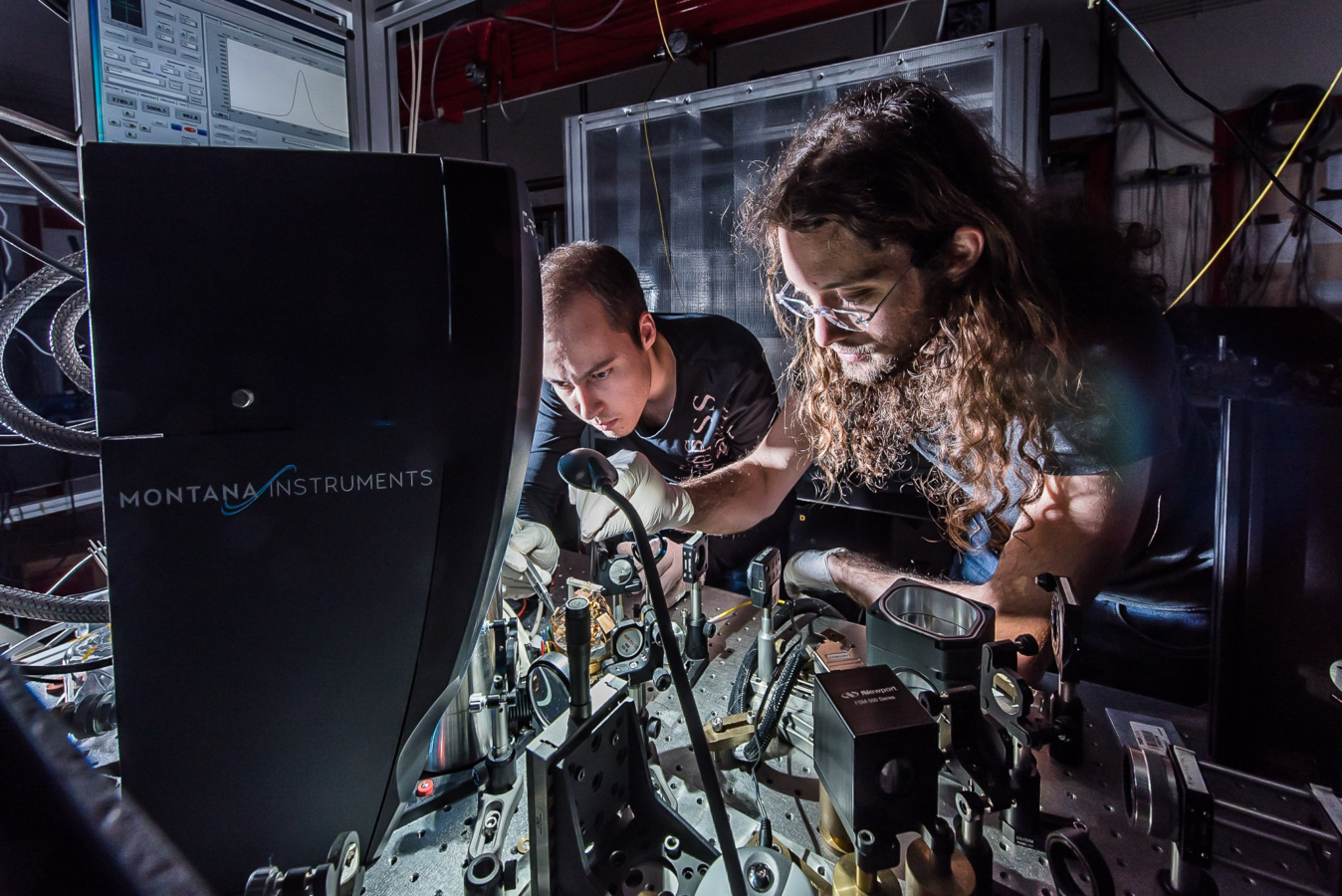 ENS. Département de physique. Doctorants théoriciens au travail Département de physique. Adrien Jeantet au premier plan devant un dispositif expérimental comprenant un crysostat et un laser servant à étudier l'emission de "grains de lumière" ou photons par des nanotubes de carbone.