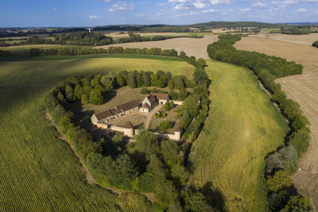 Le manoir de L'Epinay à Saint Hilaire sur Erre. Les haies épaisses qui l’entourent lui sont aujourd’hui comme une seconde enceinte. À l’abri de ses tours et de ses murs, l’Épinay semble régner sur le paysage. C’est un manoir exceptionnel, tout d’abord parce qu’en se rapprochant on comprend que le premier étage du logis est à pans de bois. Un cas unique dans le Perche. Ensuite parce que son caractère défensif, encore accentué par sa ceinture d’arbres, est probablement l’un des mieux préservé du Perche. À cela une bonne raison : l’Épinay n’est pas bâti, comme la plupart de ses semblables, sur les ruines de la guerre de Cent Ans. Le site est répertorié dès le début du XIIIe siècle. S’il ne reste rien de la bâtisse originelle, ce que nous avons sous les yeux date tout de même en grande partie de la seconde moitié du XIVe siècle. Par quel miracle a-t-il traversé la guerre sans dommages, nous l’ignorons. Mais il est toujours là, à mi-pente, orienté plein sud, comme on bâtissait à l’époque médiévale. Photographie extraite du projet photographique "les manoirs du Perche"