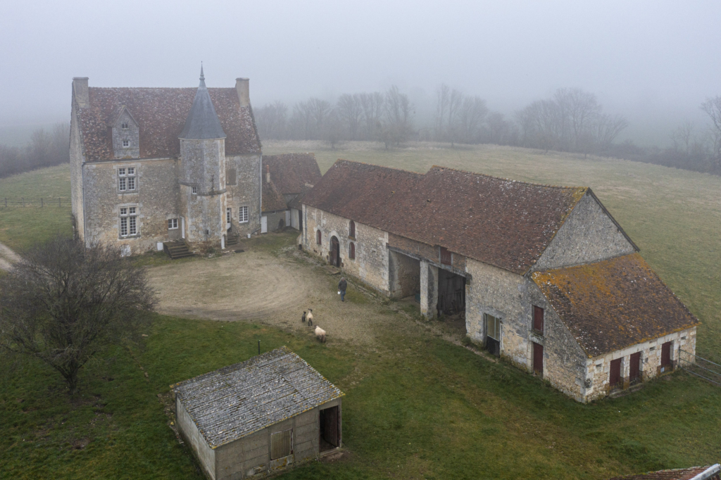 Le manoir des Rosiers à Reveillon. C’est l’un des derniers manoirs, peut-être même le dernier, à se présen- ter ainsi à nous. Le manoir des Rosiers n’a guère évolué depuis le début du XVIe siècle, époque de sa construction. C’est aujourd’hui une ferme des plus traditionnelles. La petite route qui y mène cède la place, quelques dizaines de mètres avant l’entrée, à un chemin de terre. Si l’on excepte les abris cou- verts de tôles et les marches neuves pour accéder à la porte de la tour, rien ou presque ne semble avoir changé.
Le potager, à l’avant du manoir, les pâtures et les champs de part et d’autre, témoignent d’un usage agricole immémorial. Pas de jardin d’agrément, de bordures de buis, encore moins de piscine. Les Rosiers, un manoir paysan qu’une nouvelle « noblesse » urbaine n’a pas encore converti en résidence de loisirs. Photographie extraite du projet photographique "les manoirs du Perche"
