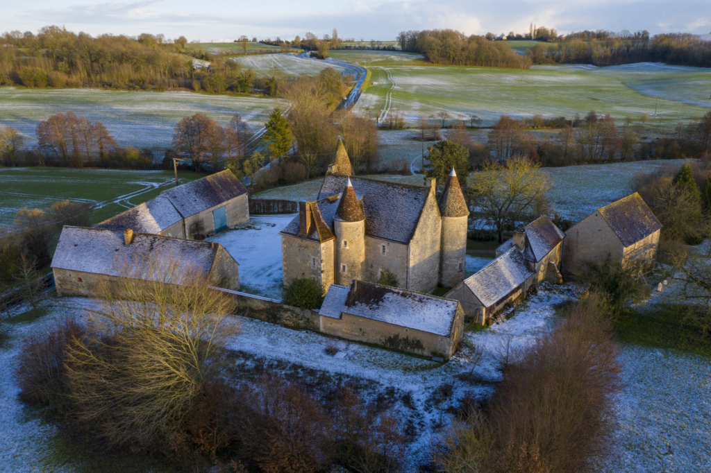 Le manoir de Lormarin à Nocé. Trapu, bien assis entre ses trois tours, entouré sur trois côtés par les bâti- ments des communs, Lormarin en impose au milieu de ce coteau qui descend lentement vers la Martinière, petit affluent de l’Erre, à deux pas de Nocé. C’est une maison relativement récente, érigée à la fin du XVIe siècle par un hobereau protestant. Il se construit alors sur un plan carré un manoir de cé- libataire, deux pièces l’une sur l’autre et deux tours. La tour d’escalier à l’ar- rière et la grosse tour de guet à l’avant. Le mariage du propriétaire, dix ans plus tard, l’amènera à doubler la superficie du manoir qui de carré deviendra rectangle avec l’adjonction d’une troisième tour en façade. Un siècle plus tard, la révocation de l’Édit de Nantes mettra un coup d’arrêt définitif aux travaux d’agrandissement poursuivis par les héritiers du premier bâtisseur.
Lormarin a gardé de ses origines cette modestie rurale dans les extérieurs. Un potager, des arbres fruitiers, une cour en herbe jusqu’au pied des murs. Les propriétaires actuels ont reboisé les abords immédiats, totalement nus lorsqu’ils sont arrivés il y a vingt-cinq ans. Hélas, ils n’ont rien pu faire pour les six cents pommiers présents dans les champs alentour et qui ont disparu, victimes de la mécanisation et du remembrement. Photographie extraite du projet photographique "les manoirs du Perche"