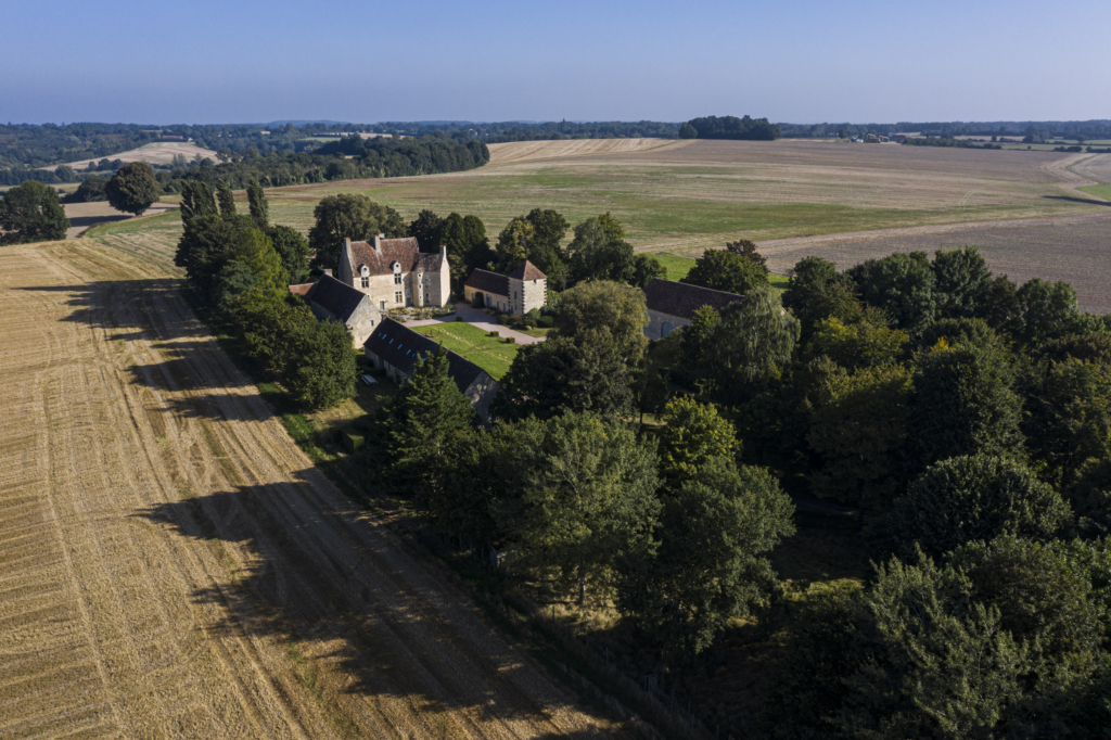 Le manoir de Soisay à La Perrière. Il est le dernier témoignage d’un paysage disparu. Des bois, des haies, des vergers qui jadis couvraient la hauteur sur laquelle il s’élance ne subsiste plus grand chose. Nous sommes aux confins du Perche, à la limite de la Sarthe, gagnés par des pratiques agricoles industrielles. Et voilà Soisay esseulé au milieu d’immenses parcelles. Le manoir domine à l’ouest le Saosnois. À l’est le paysage descend lentement vers le bourg de La Perrière.
Comme très souvent dans le Perche, le manoir actuel, construit dans la première moitié du XVIe siècle, a succédé à une place forte médiévale dont il ne reste aucun vestige.
C’est un grand manoir, transformé jusqu’au XVIIIe siècle par l’adjonction d’importants bâtiments agricoles, qui s’offre aujourd’hui à nous. La taille des communs dit assez l’importance de l’exploitation dont Soisay a été le siège jusqu’en 1978. À cette époque, les cultures arrivaient jusqu’au ras des murs. Depuis, les propriétaires successifs ont entrepris de planter des arbres, un parc qui aujourd’hui l’encadre et le protège harmonieusement.
Dès le début du XXIe siècle son usage a évolué avec l’arrivée de nouveaux propriétaires. C’est ainsi que désormais, le pré à droite du manoir, qui fut aussi pendant des années une piste pour ULM, sert, tout comme la cour, de cadre à des expositions d’art contemporain. Photographie extraite du projet photographique "les manoirs du Perche"